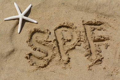 Photo of Abbreviation SPF written on sand and starfish at beach, above view