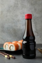 Bottle of tasty soy sauce, chopsticks and sushi rolls with salmon on grey table