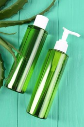 Photo of Bottles of cosmetic gel with aloe extract and fresh leaves on light green wooden table, flat lay