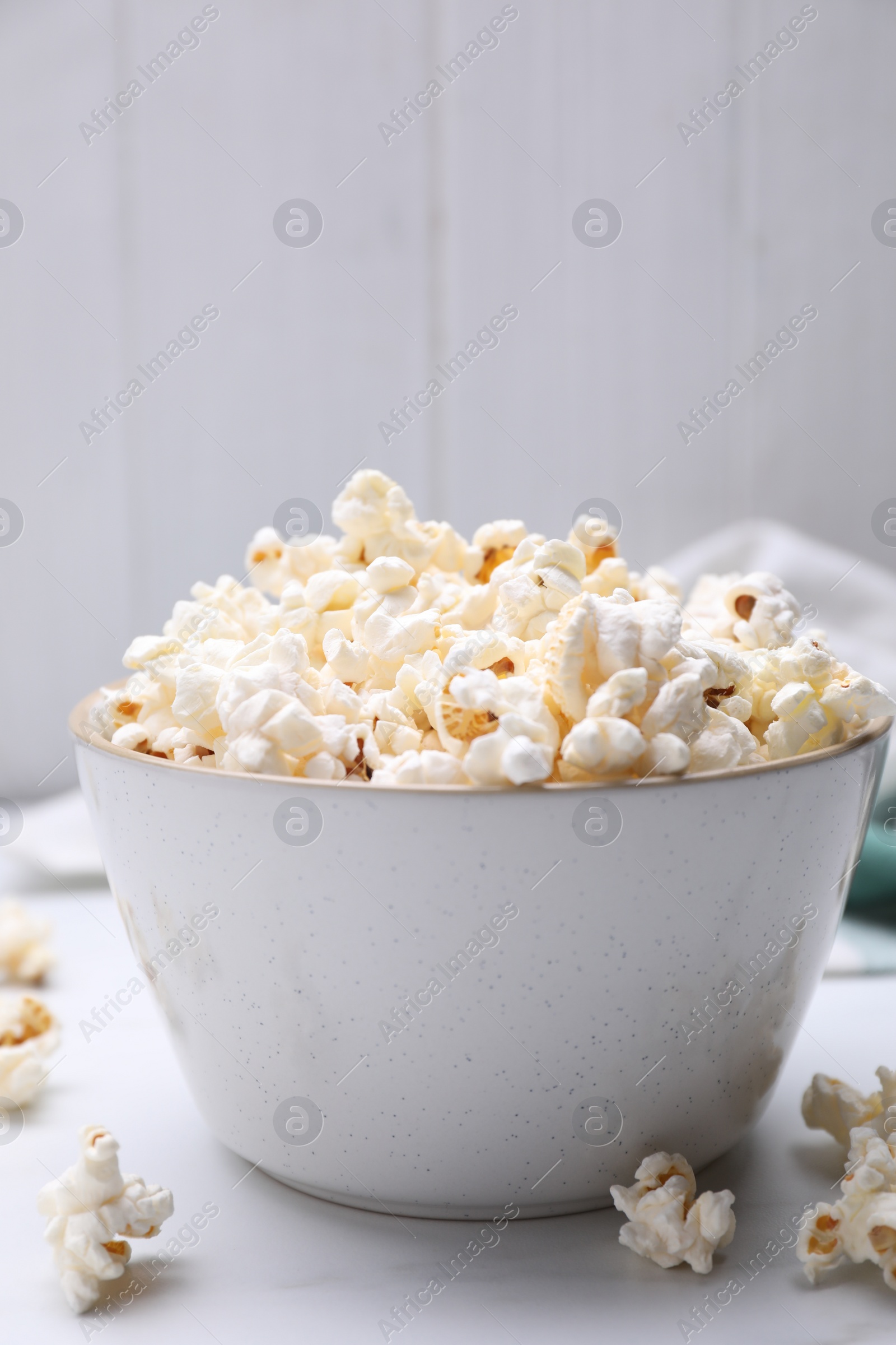 Photo of Bowl of tasty popcorn on white table, closeup