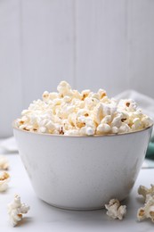 Photo of Bowl of tasty popcorn on white table, closeup