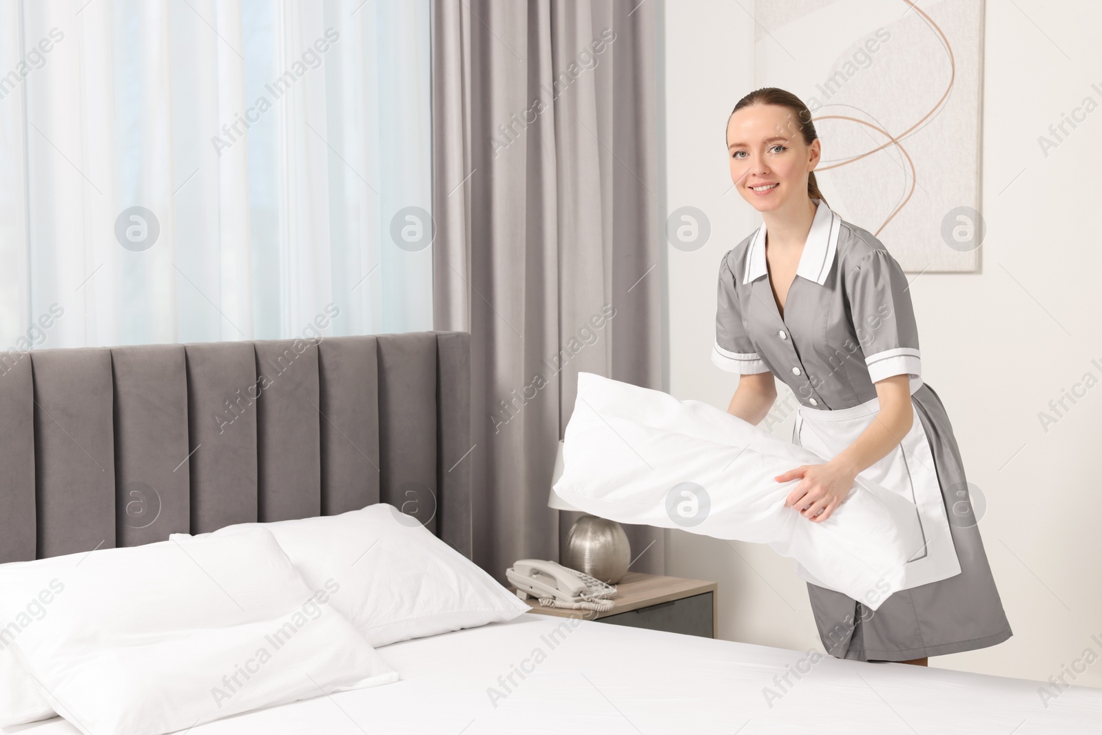 Photo of Young maid making bed in hotel room. Space for text