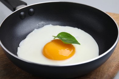 Photo of Pan with tasty fried egg on wooden board, closeup