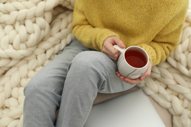 Photo of Woman with cup of tea sitting near plaid, closeup