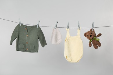 Photo of Different baby clothes and toy drying on laundry line against light background