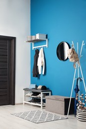 Photo of Stylish hallway with coat rack and shoe storage bench near blue wall. Interior design