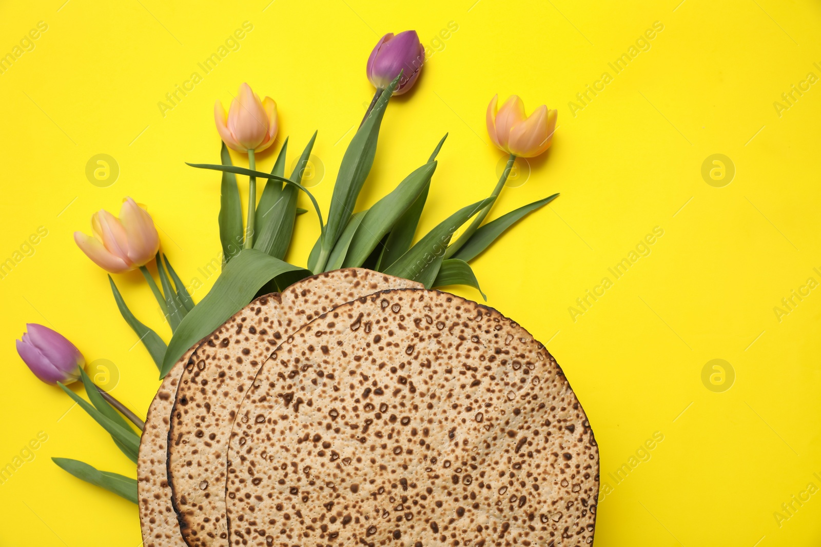 Photo of Tasty matzos and fresh flowers on yellow background, flat lay. Passover (Pesach) celebration