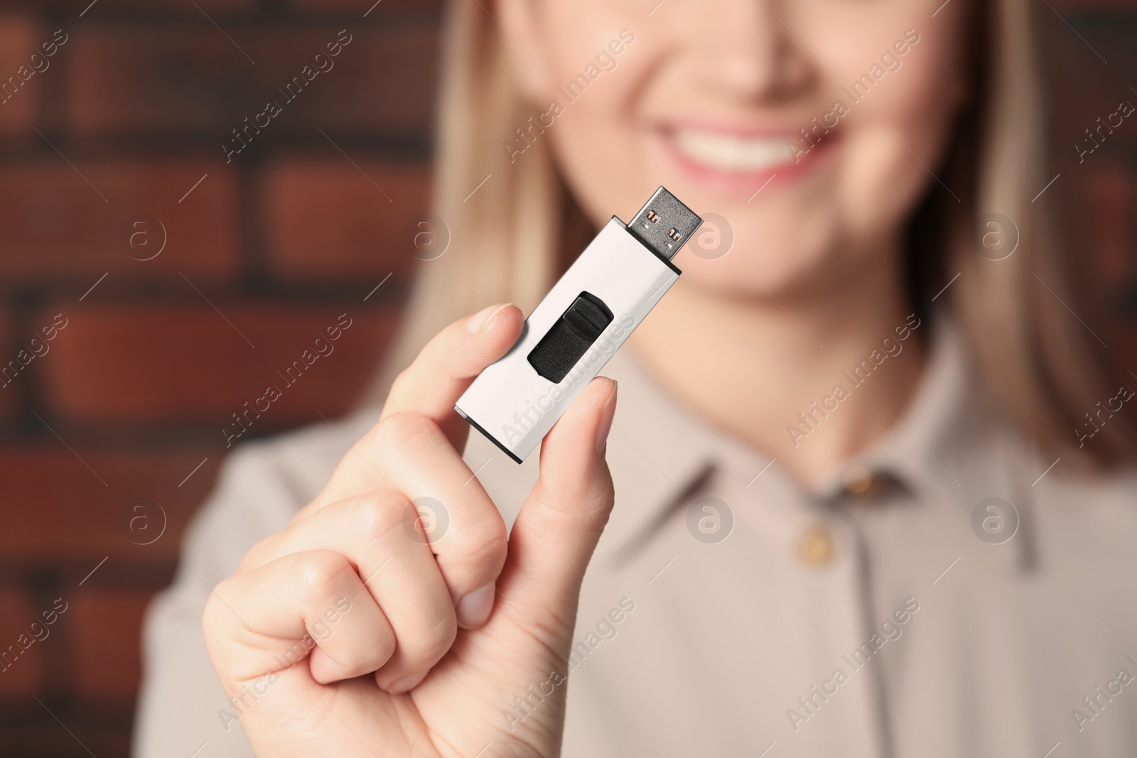 Photo of Woman holding usb flash drive near brick wall, focus on hand