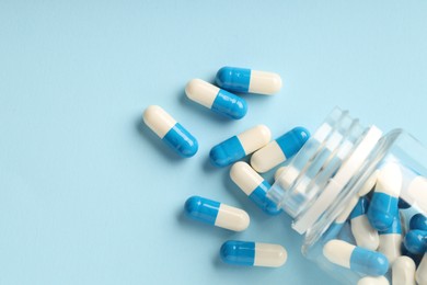 Photo of Antibiotic pills and bottle on light blue background, top view. Space for text