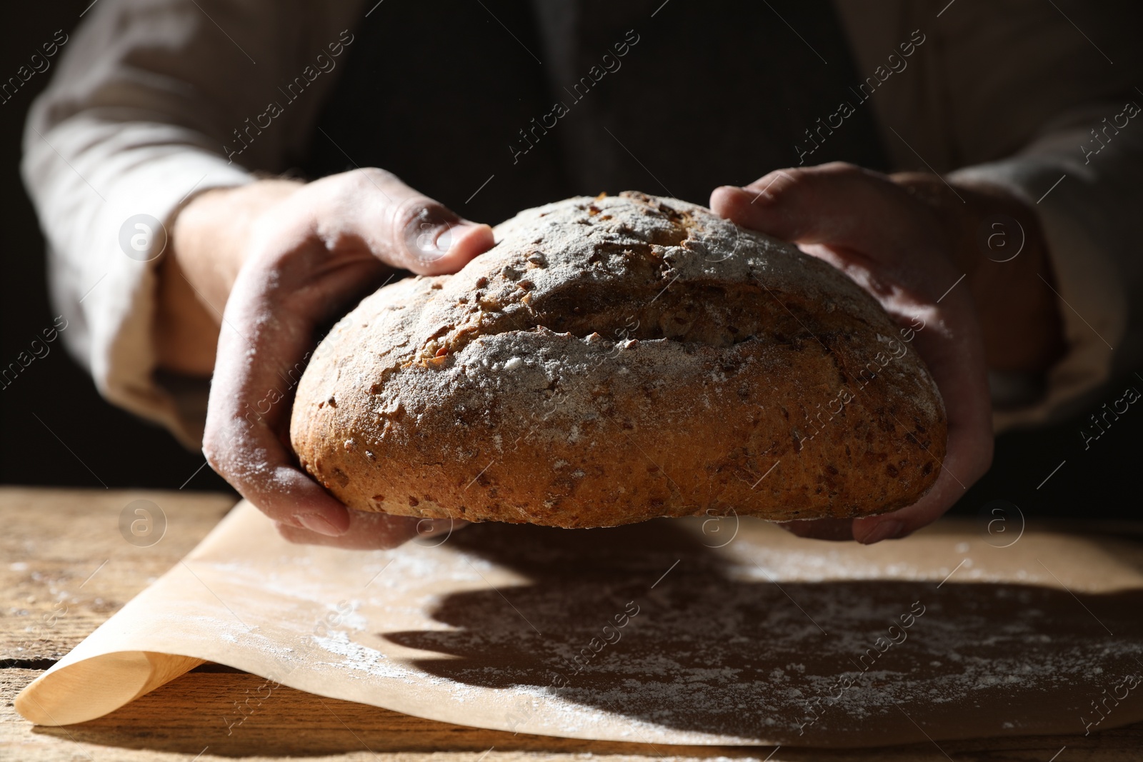 Photo of Man breaking loaf of fresh bread at wooden table, closeup