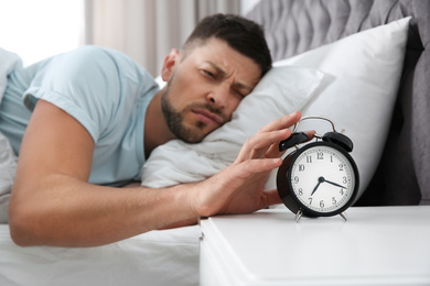 Photo of Sleepy man turning off alarm clock at home in morning, focus on hand