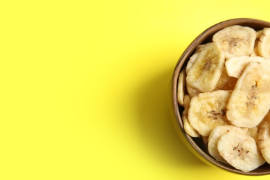 Photo of Wooden bowl with sweet banana slices on color background, top view with space for text. Dried fruit as healthy snack