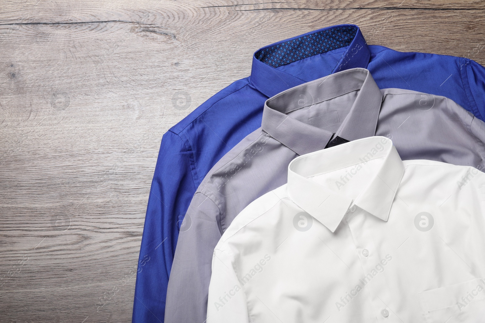 Photo of Stylish shirts on wooden table, flat lay. Dry-cleaning service