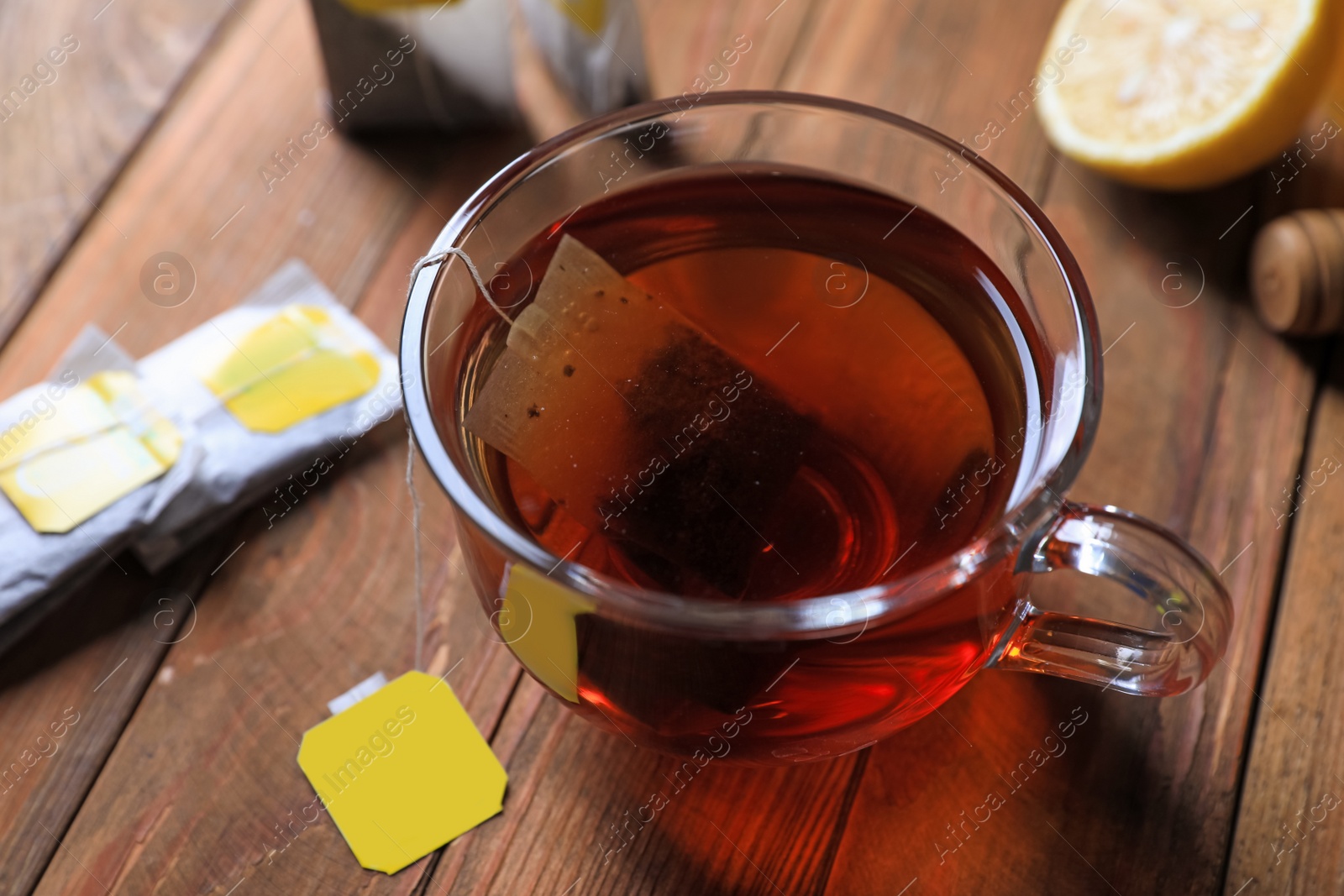 Photo of Tea bag in glass cup on wooden table, closeup