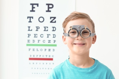 Photo of Little boy with trial frame near eye chart in ophthalmologist office