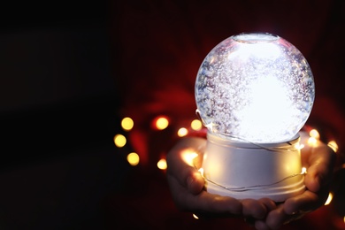 Photo of Woman holding snow globe and Christmas lights, closeup. Space for text