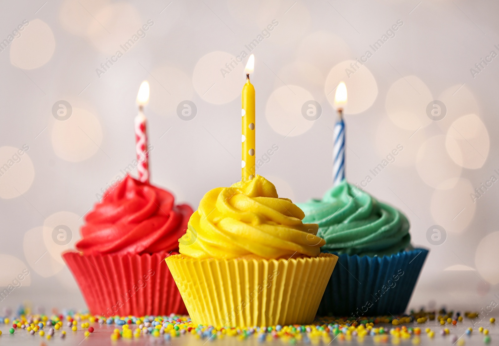 Photo of Delicious birthday cupcakes with burning candles on table