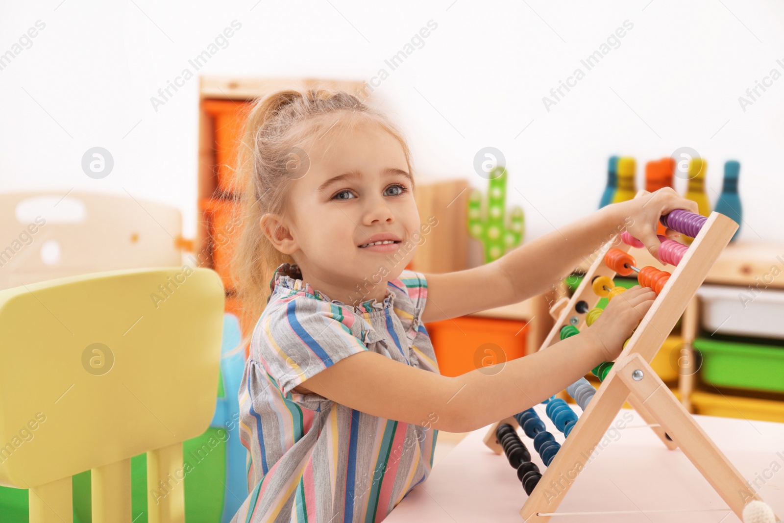 Photo of Cute child playing with wooden abacus at table in room