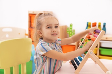 Photo of Cute child playing with wooden abacus at table in room