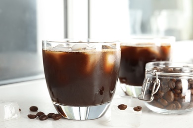 Photo of Glass of coffee drink with ice cubes and beans in jar on table