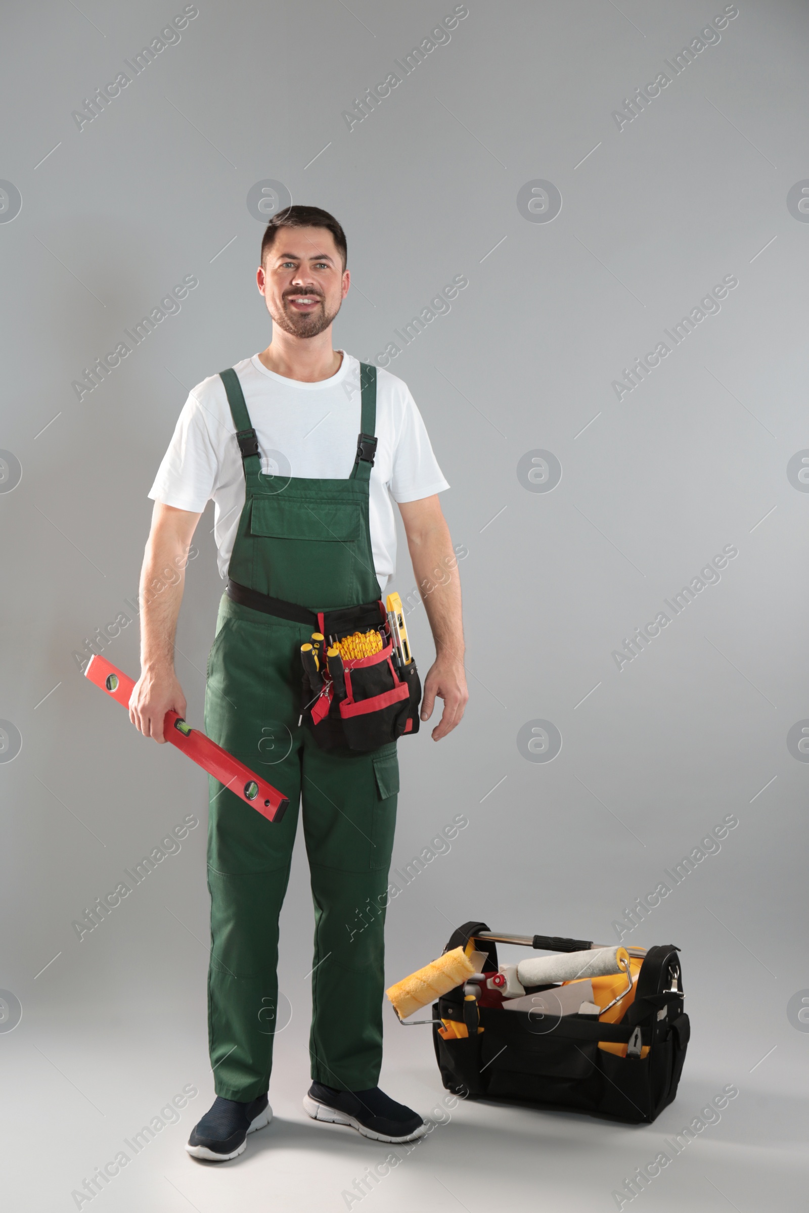 Photo of Full length portrait of professional construction worker with tools on grey background