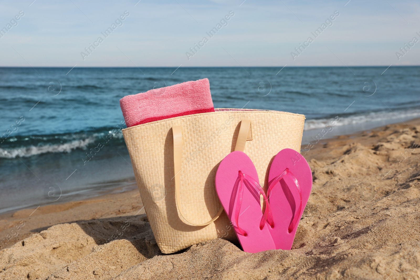 Photo of Summer bag with slippers and beach towel on sand near sea
