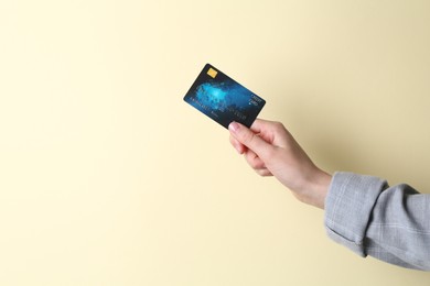 Woman holding credit card on beige background, closeup