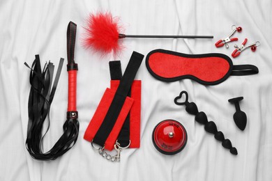 Photo of Sex toys and accessories on white fabric, flat lay