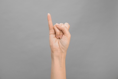 Photo of Woman showing I letter on grey background, closeup. Sign language