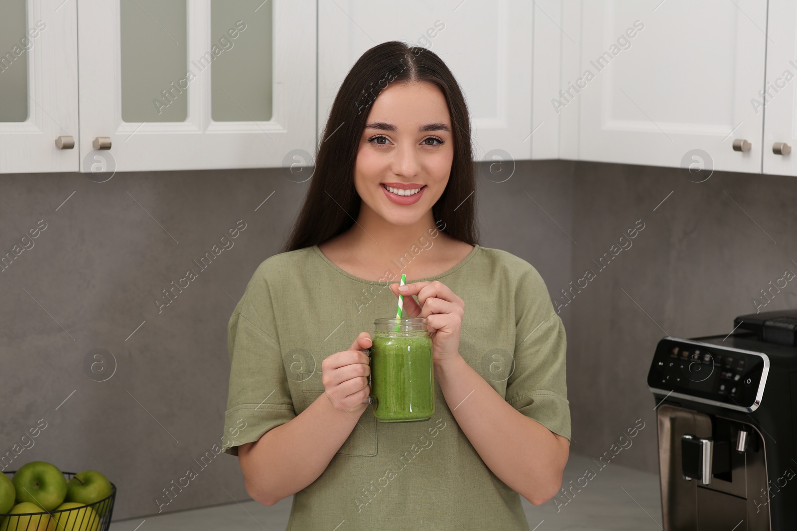 Photo of Beautiful young woman holding mason jar with delicious smoothie in kitchen