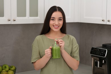 Beautiful young woman holding mason jar with delicious smoothie in kitchen