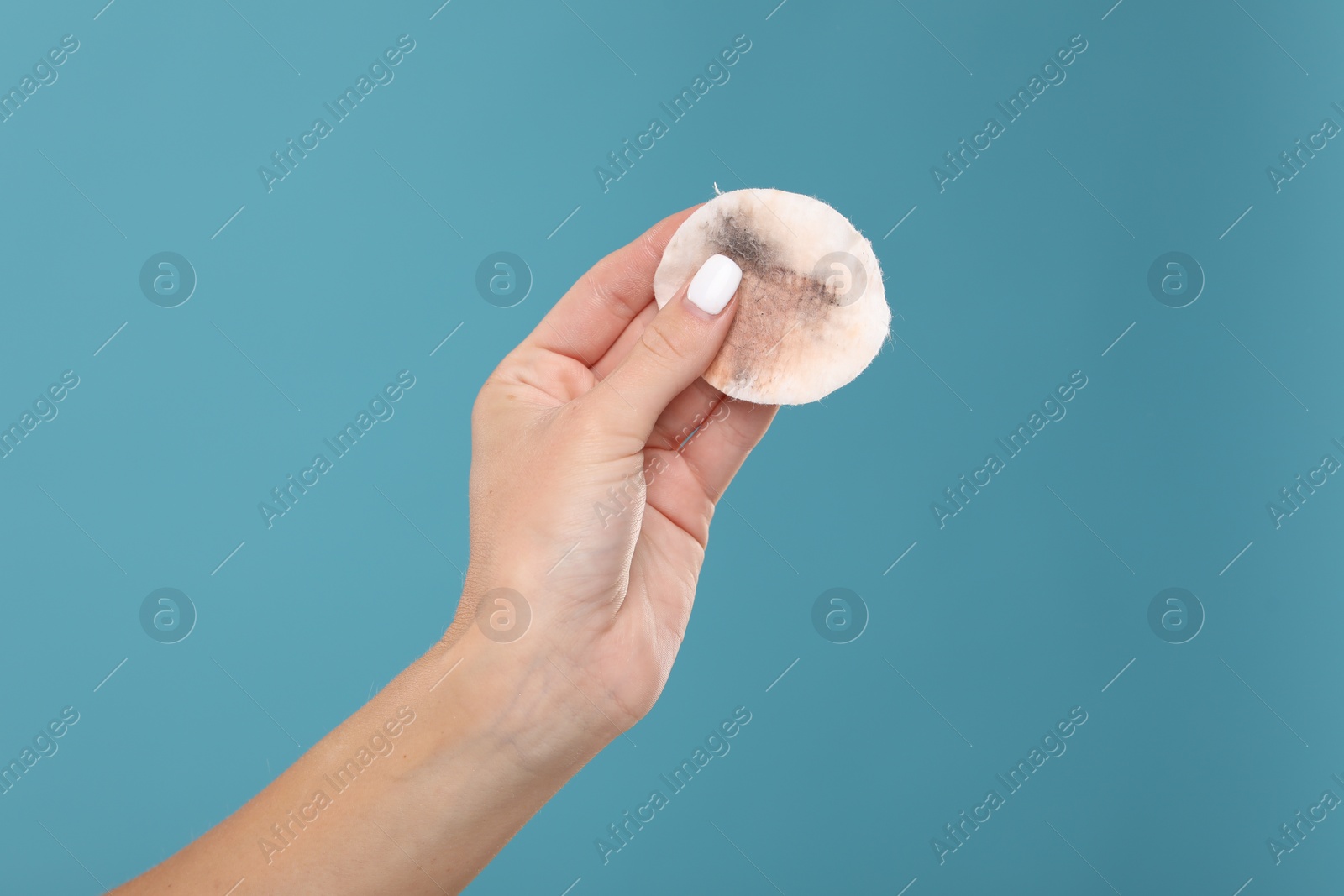 Photo of Woman with dirty cotton pad after removing makeup on light blue background, closeup