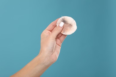 Woman with dirty cotton pad after removing makeup on light blue background, closeup