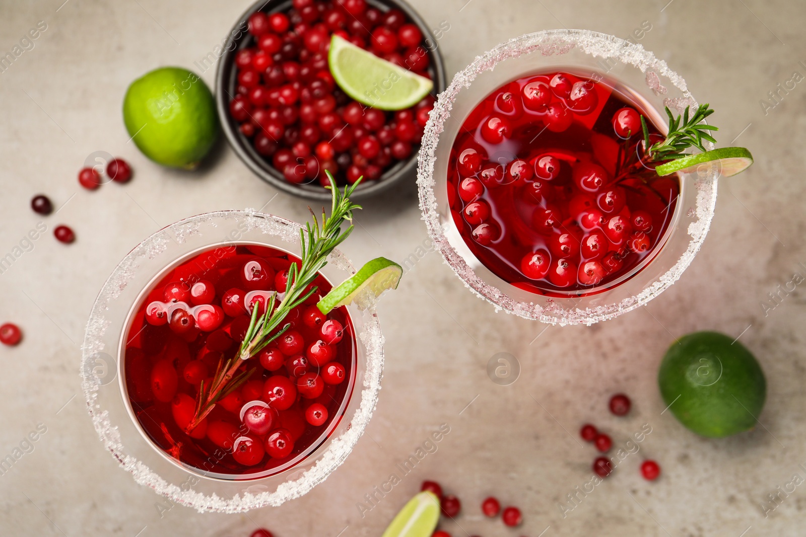 Photo of Tasty cranberry cocktail with rosemary and lime in glasses on grey table, flat lay