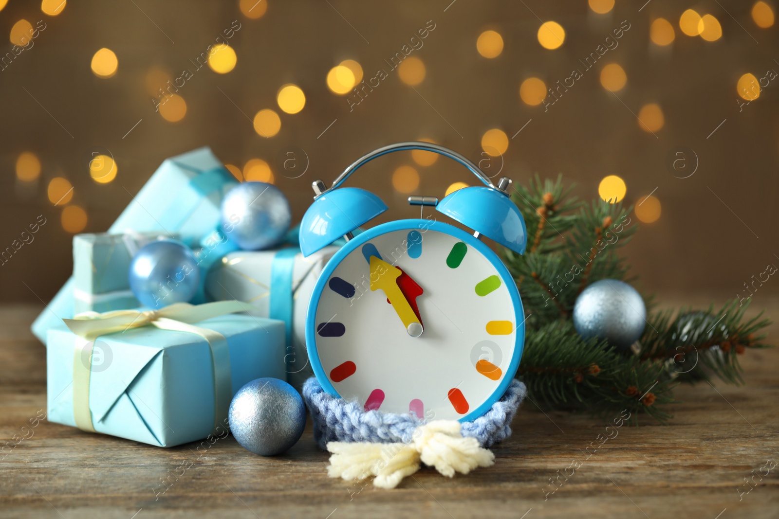 Photo of Alarm clock with decor on wooden table against blurred Christmas lights, closeup. New Year countdown