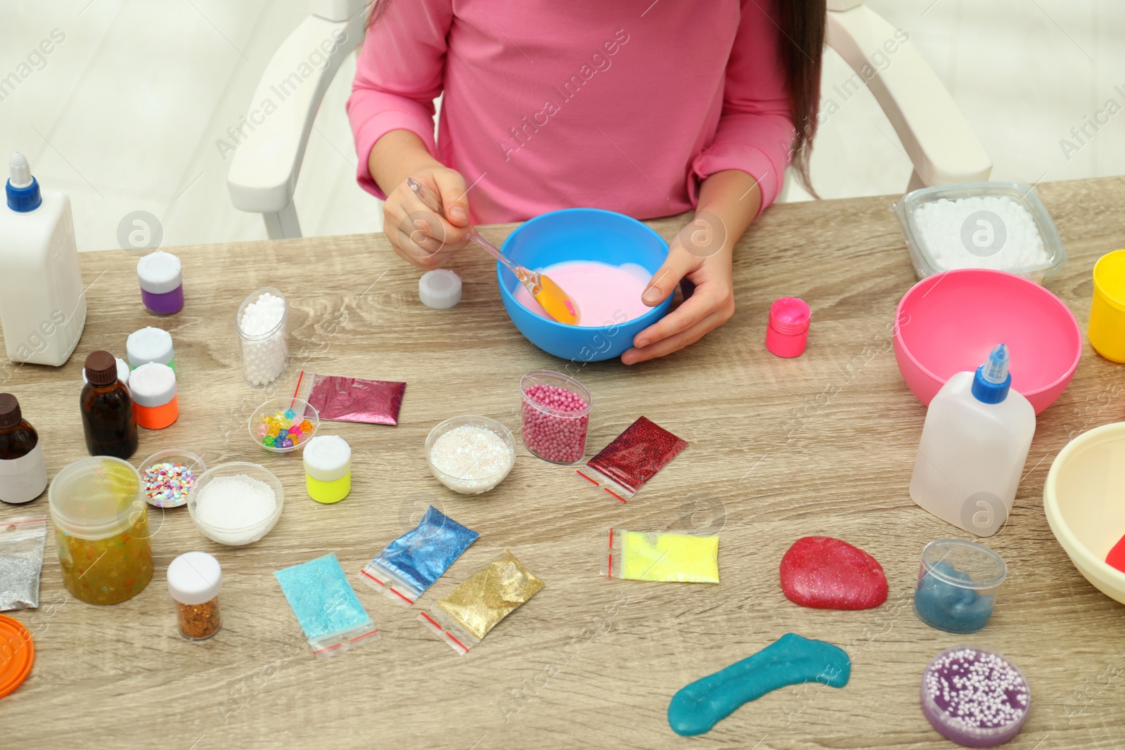 Photo of Little girl mixing ingredients with silicone spatula at table, closeup. DIY slime toy