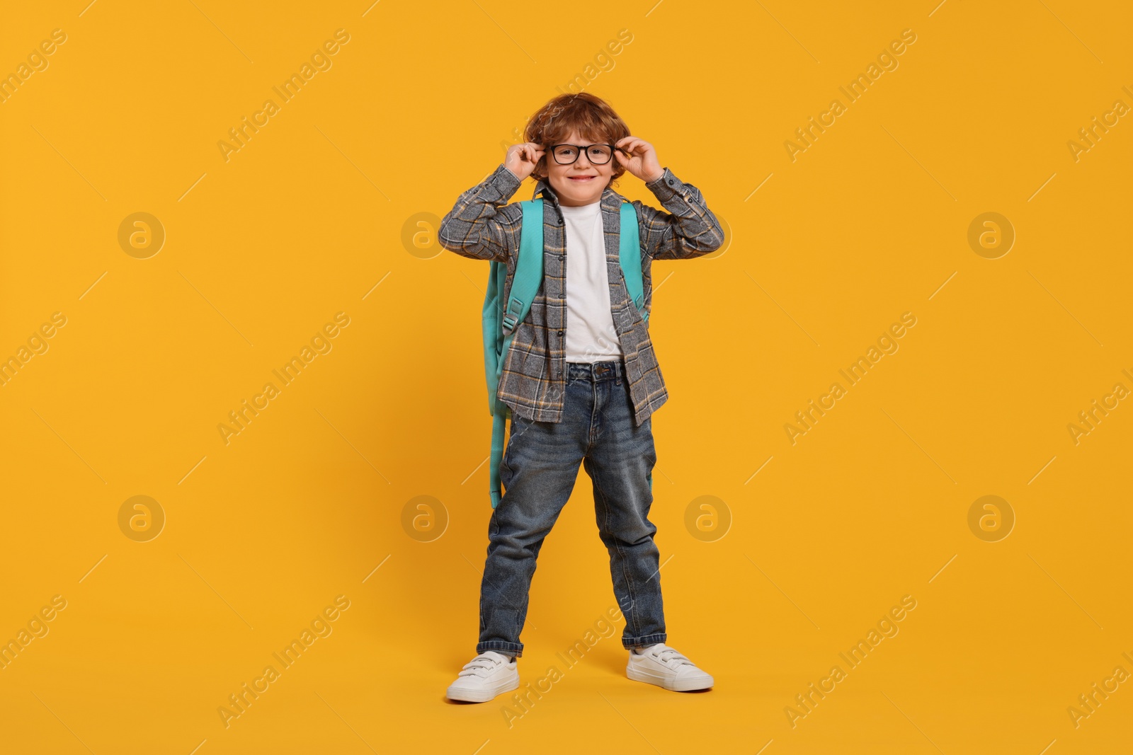 Photo of Happy schoolboy with backpack on orange background