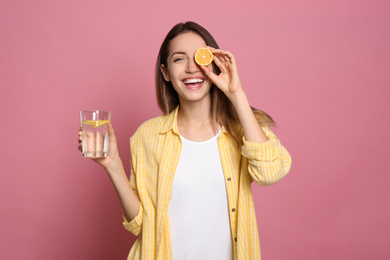 Photo of Young woman with glass of lemon water on pink background