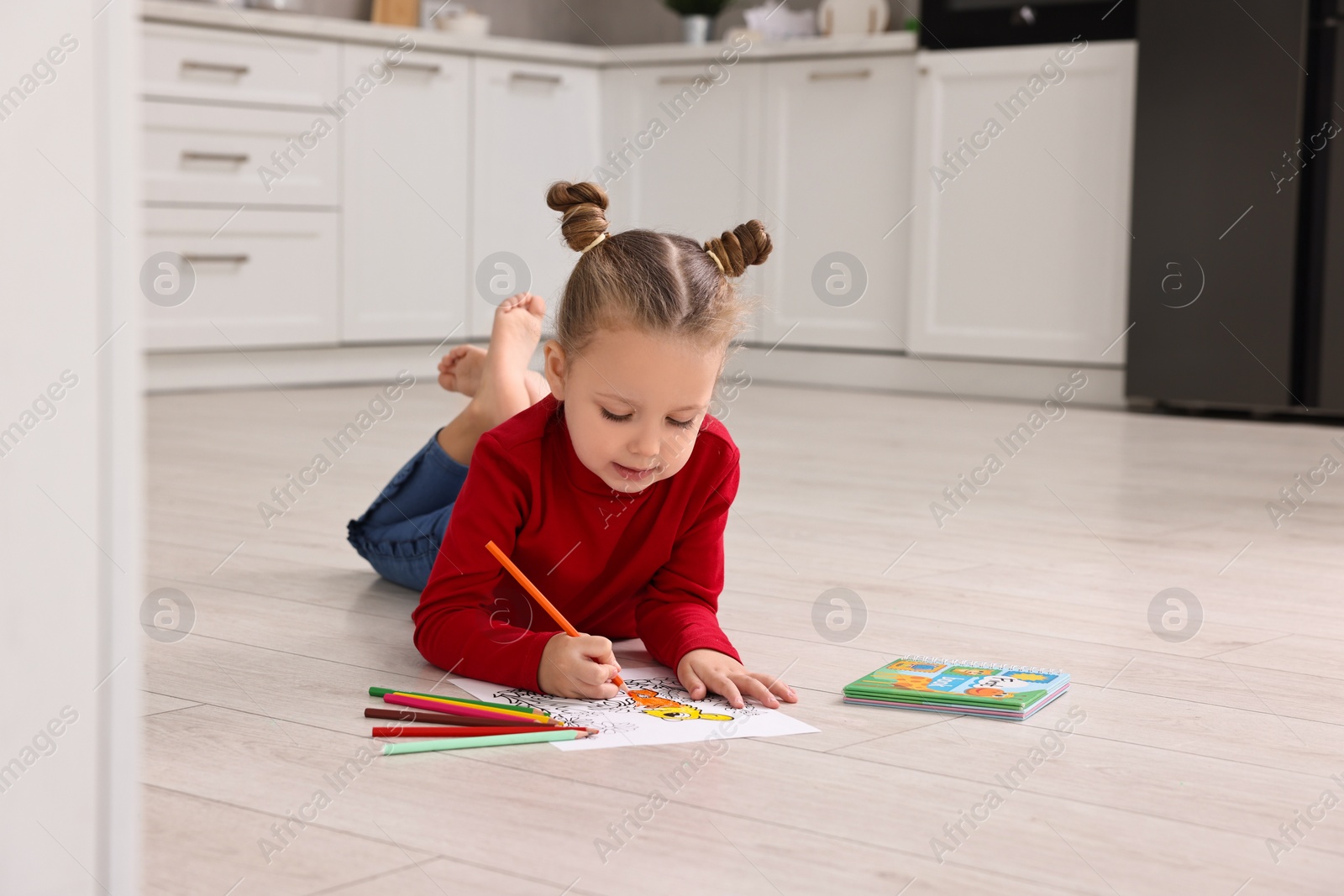 Photo of Cute little girl coloring drawing on warm floor in kitchen. Heating system