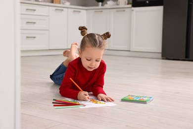Photo of Cute little girl coloring drawing on warm floor in kitchen. Heating system