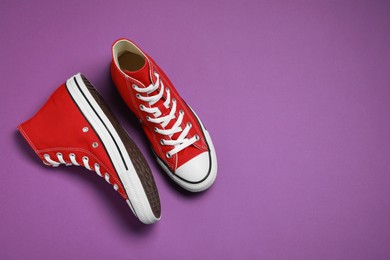 Photo of Pair of new stylish red sneakers on purple background, flat lay. Space for text