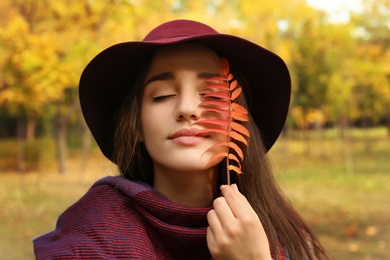 Young beautiful woman with hat and leaf in park. Autumn walk