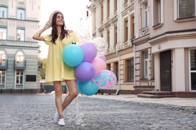 Photo of Beautiful young woman with color balloons on city street