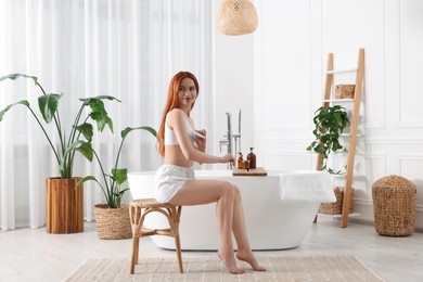 Photo of Beautiful young woman applying body cream onto arms in bathroom, space for text