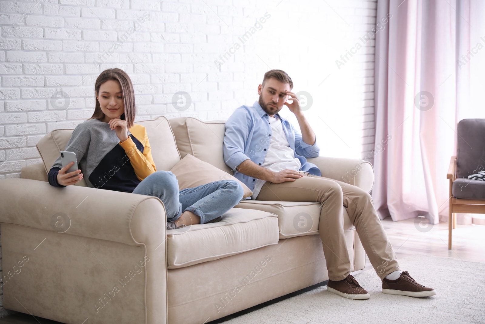 Photo of Young man peering into girlfriend's smartphone at home. Relationship problems