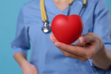 Photo of Doctor holding red heart on light blue background, closeup. Cardiology concept