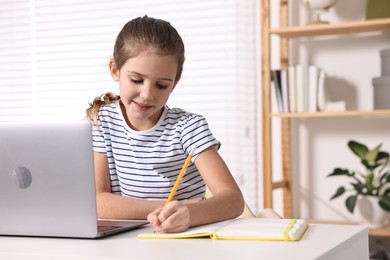 Photo of E-learning. Cute girl taking notes during online lesson at table indoors