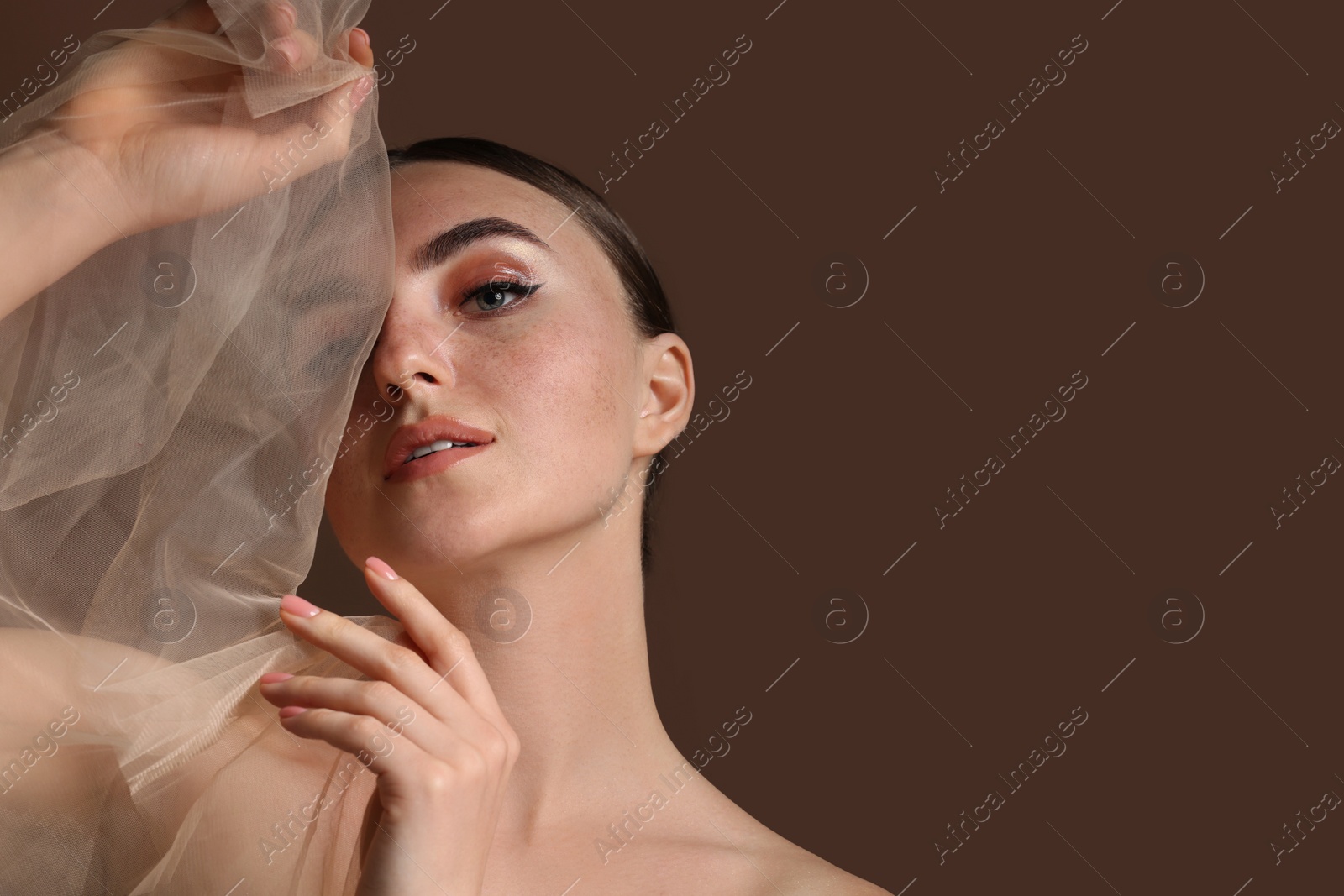 Photo of Fashionable portrait of beautiful woman with fake freckles on brown background. Space for text