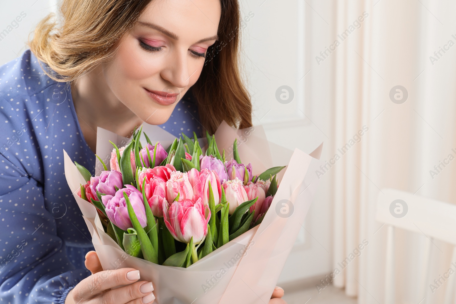 Photo of Young woman with bouquet of beautiful tulips indoors. Space for text