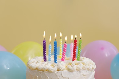 Photo of Delicious cake with burning candles and festive decor on yellow background, closeup